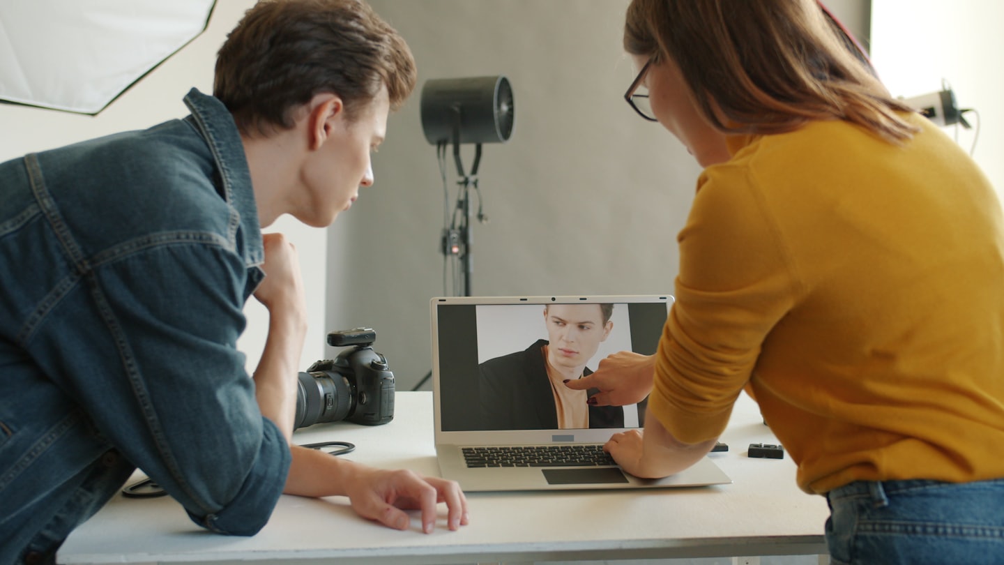 Två fotografer samarbetar över en laptop i en studio.