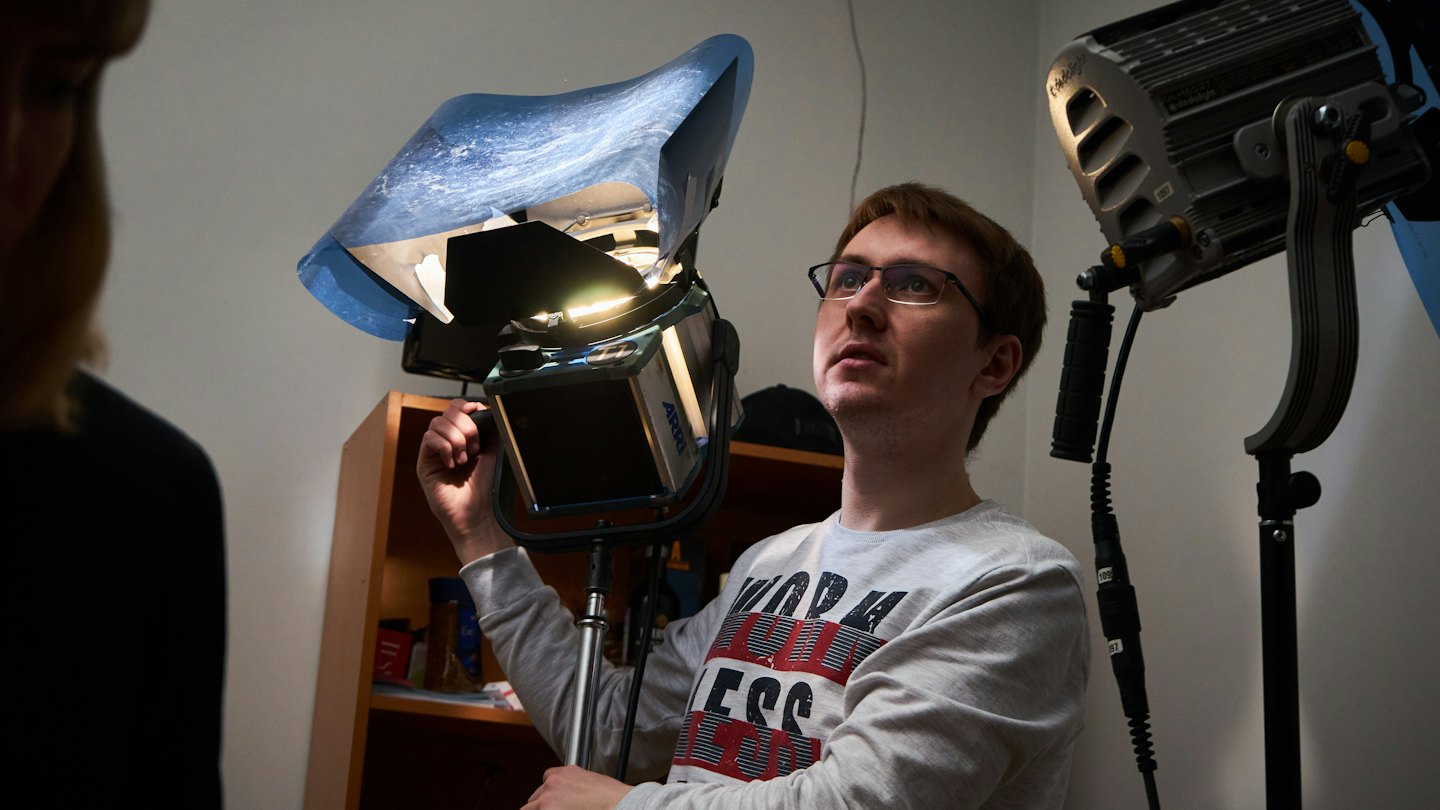 Man i grå sweatshirt justerar studiolampa med blå diffuser.